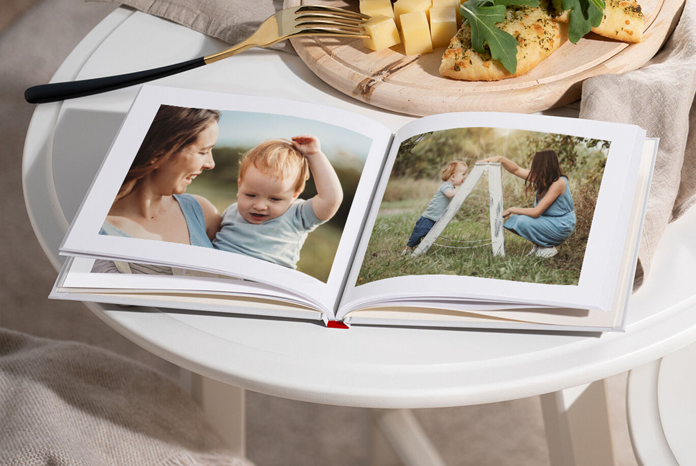 Ein offenes Fotobuch auf einem Tisch. Auf der linken Seite sind zwei Bilder, die eine Mutter und ihr Kind zeigen. Auf der rechten Seite sieht man eine Frau, die mit einem Kind spielt. Der Tisch ist dekoriert mit einer Holzteller, auf dem Brot und frischer