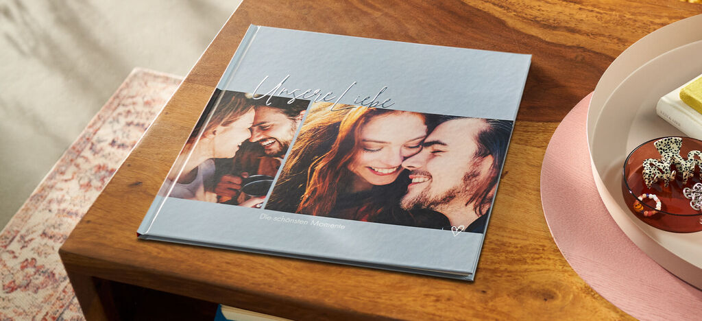 Ein CEWE FOTOBUCH liegt auf einem holzähnlichen Tisch und zeigt liebevolle Momente mit Personen.