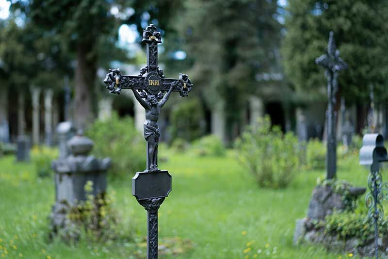 Schwarzes Kreuz mit Jesusfigur auf einem Friedhof umgeben von grünem Gras
