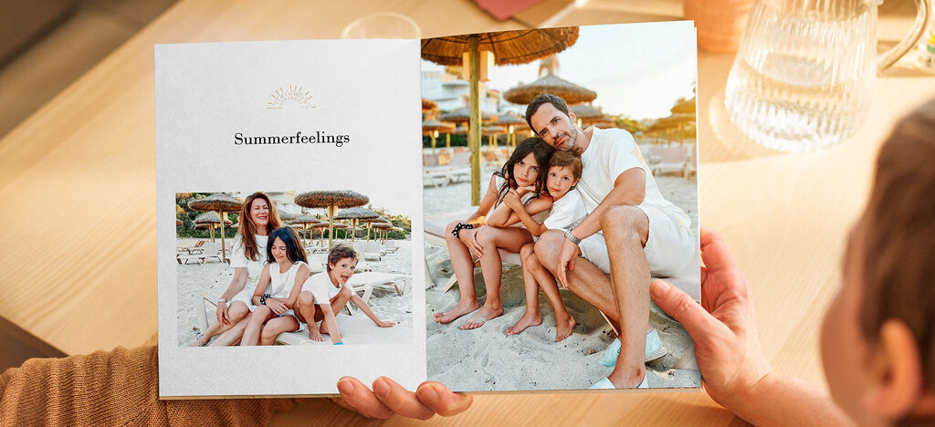 Familie blickt lächelnd in ein CEWE FOTOBUCH mit Urlaubsbildern am Strand.