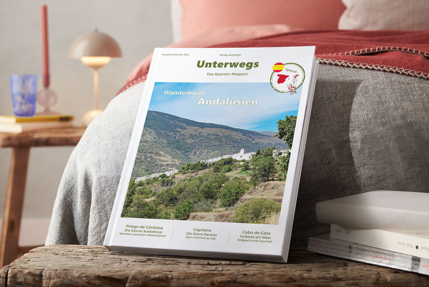 Ein Reisemagazin mit dem Titel "Unterwegs - Das Spanien Magazin" liegt auf einem Holztisch. Es zeigt eine Landschaft aus Andalusien.