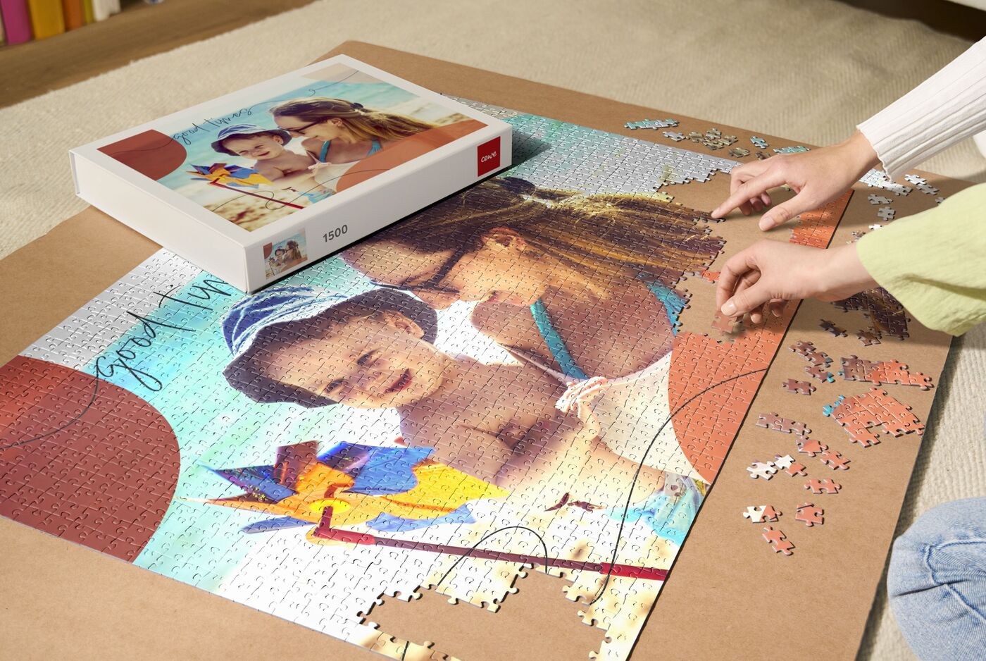 Eine Mutter und ihr Kind legen ein Puzzle mit einem bunten Strandmotiv auf einen Tisch. Die Puzzlebox ist ebenfalls sichtbar.