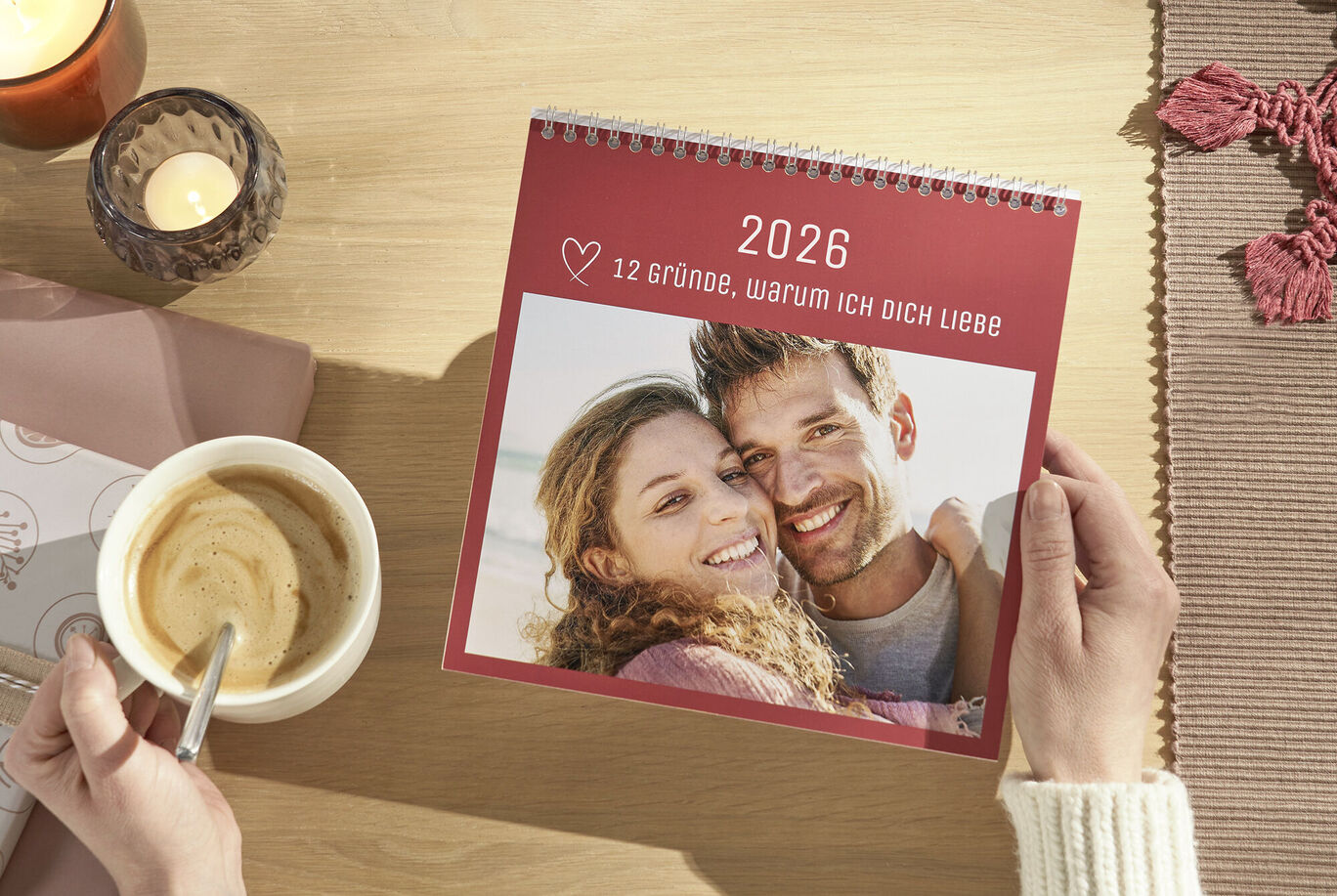 Person hält einen CEWE Fotokalender mit 12 Gründen, warum sie jemanden liebt, am Tisch.