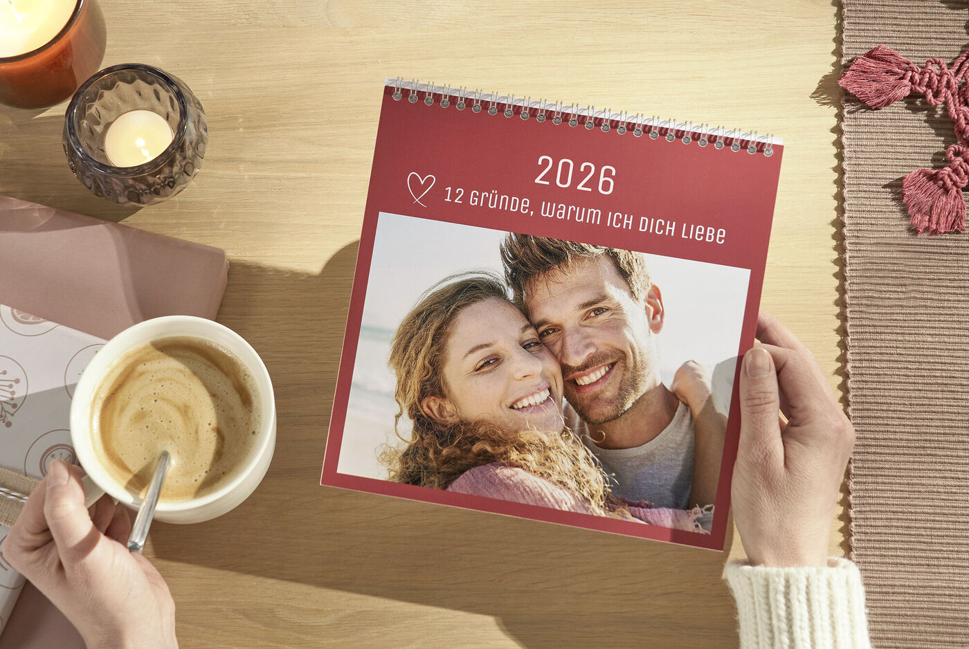 Person hält einen CEWE Fotokalender mit 12 Gründen, warum sie jemanden liebt, am Tisch.