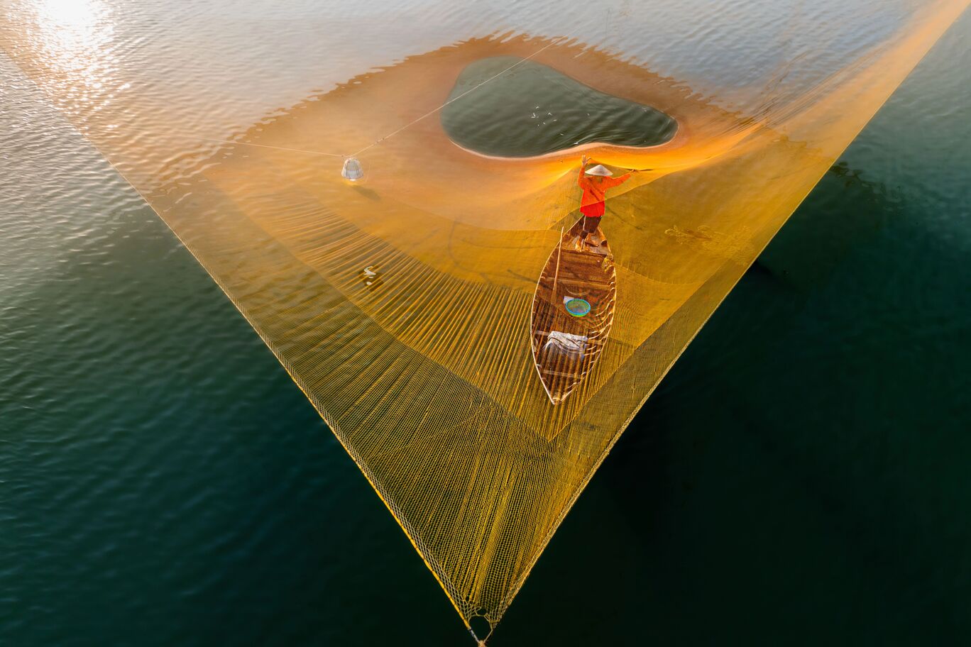 Person in einem Boot wirft ein Netz ins Wasser.