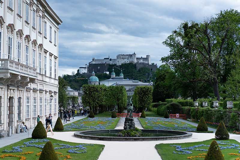Schöner Garten mit einem Brunnen, im Hintergrund die Burg Hohensalzburg in Salzburg.