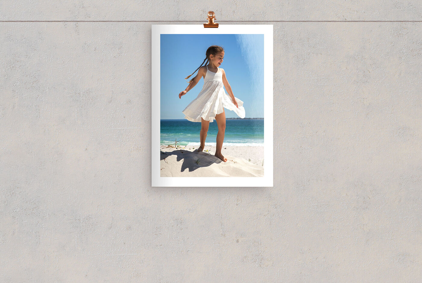 Ein fröhliches Mädchen in einem weißen Kleid, das am Strand steht, umgeben von Sand und Meer unter blauem Himmel.