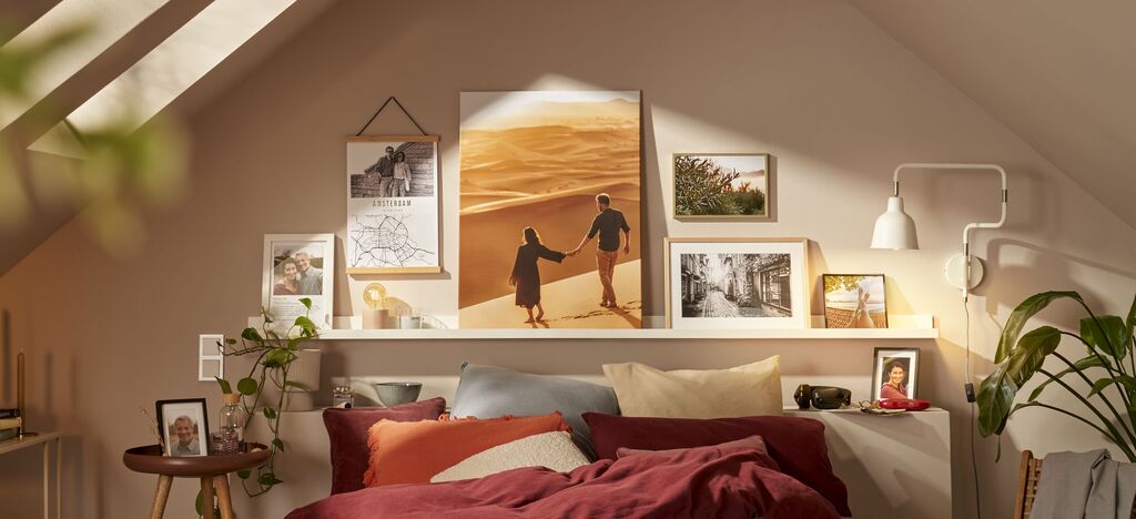 Ein gemütliches Schlafzimmer mit einem großem CEWE Wandbild und mehreren Bildern auf einem Regal.