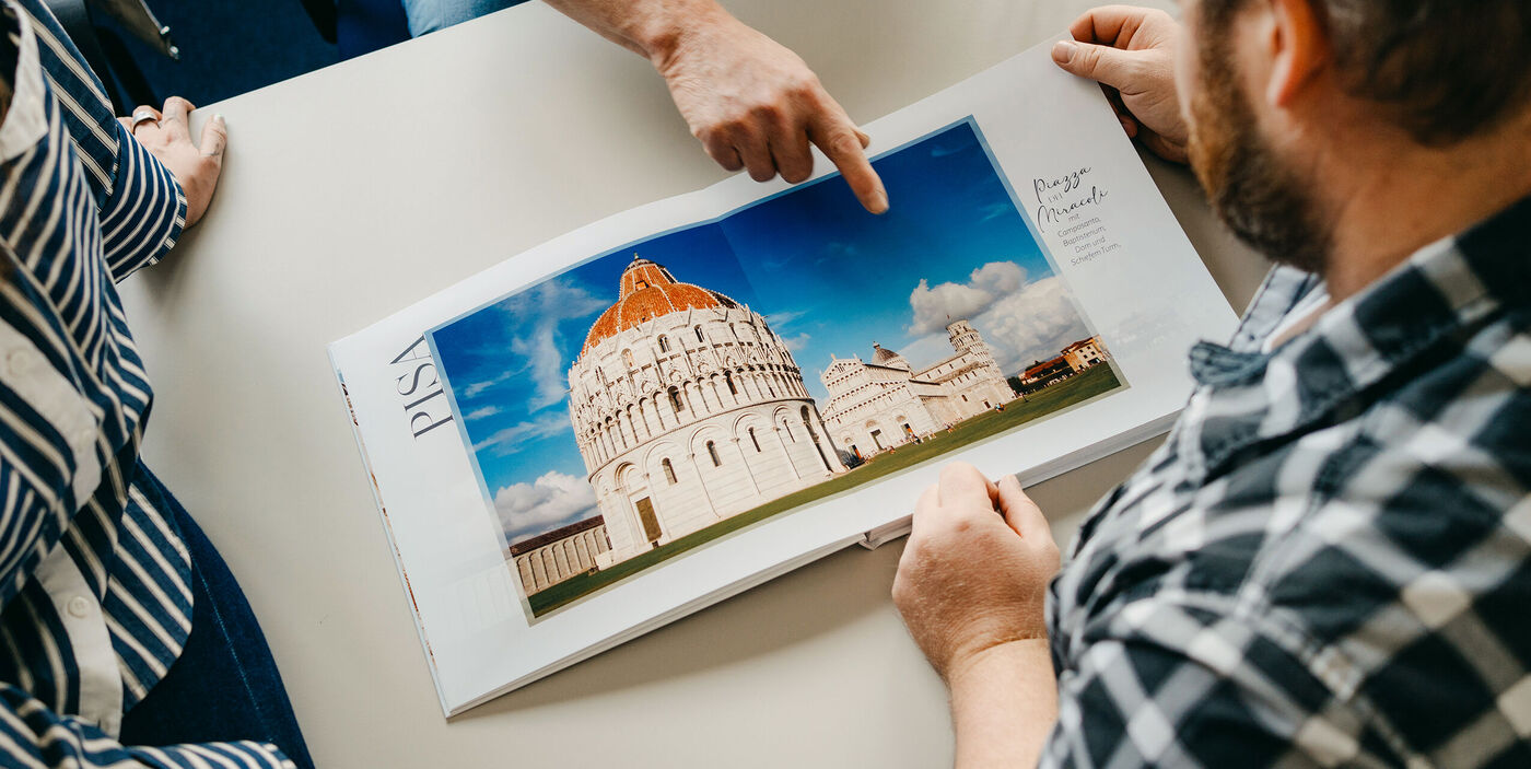 Zwei Personen betrachten ein CEWE FOTOBUCH mit einer Reisefotografie vom Schiefen Turm und der Kathedrale in Pisa