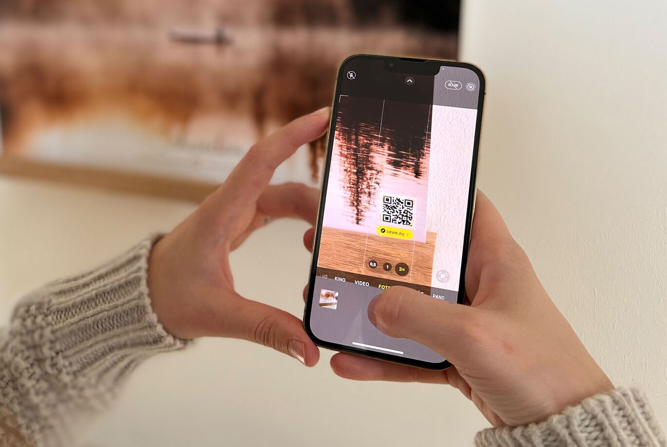 Eine Person scannt mit einem Smartphone einen QR-Code an einer Wand. Die Wand hat ein schönes Bild.