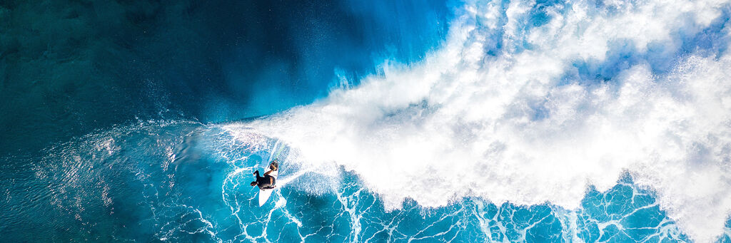 Ein Surfer reitet über einer Welle im türkisfarbenen Wasser, umgeben von schäumenden Wellen.