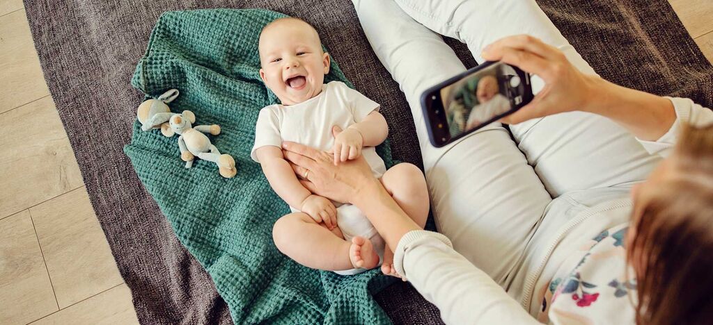 Eine liebevolle Mutter macht ein Foto von ihrem Baby auf einer Decke, während ein Spielzeug daneben liegt