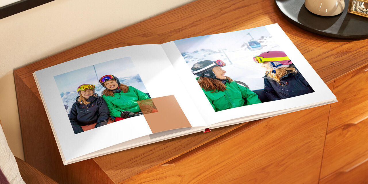 Ein offenes CEWE Fotobuch mit fröhlichen Fotos von zwei Personen, die Ski fahren.