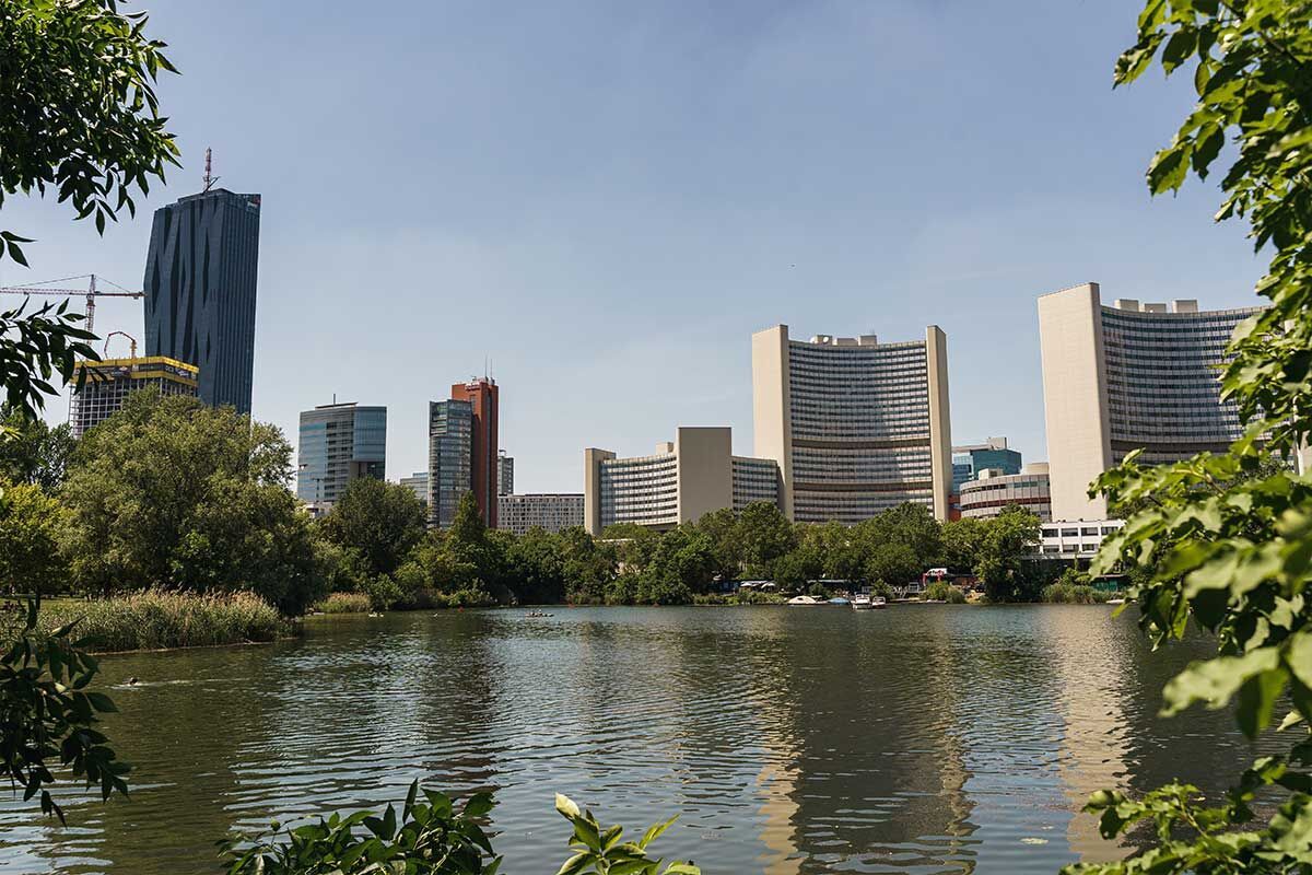 Blick auf die moderne Skyline von Wien am Ufer eines ruhigen Sees, umgeben von grünen Bäumen