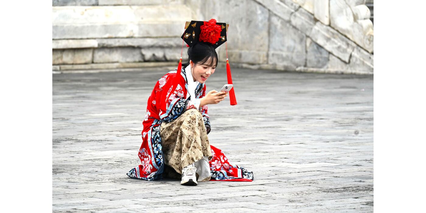 Ein junges Mädchen gekleidet in einem traditionellen asiatischen Gewand kniend auf einem Platz mit einem Smartphone in der Hand