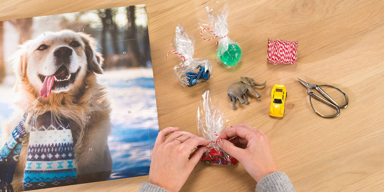 Eine Person bindet Geschenke mit buntem Garn auf einem Tisch mit einem Hundebild im Hintergrund