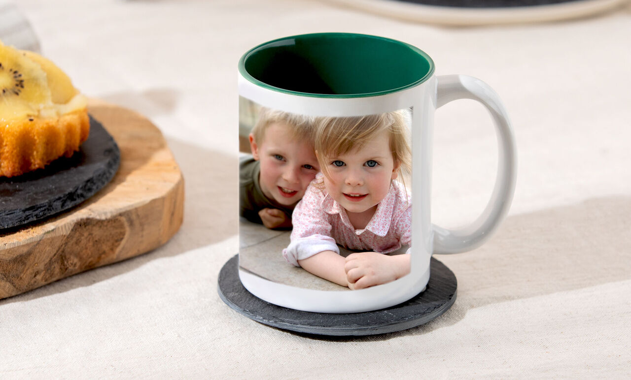 Panorama-Fototasse mit Innenfarbe in Grün auf einem Tisch. Auf der Tasse ist ein Foto von zwei Kindern, die in die Kamera lächeln.