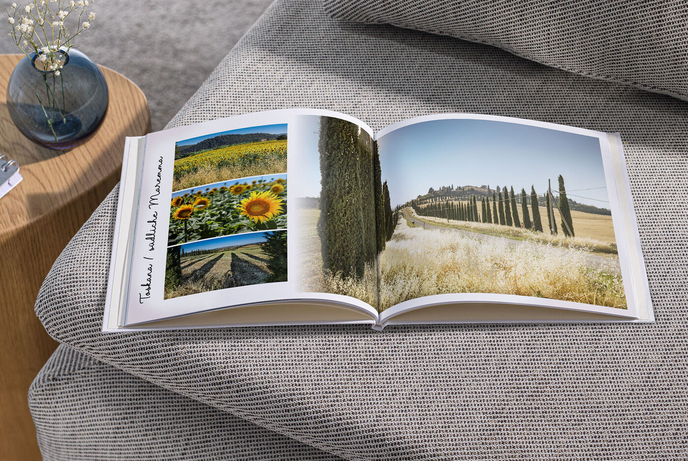 Ein offenes Fotobuch auf einer Couch zeigt Landschaften mit Sonnenblumen und Zypressen.