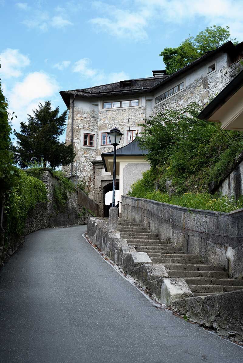 Eine malerische Gasse führt zu einem charmanten, historischen Gebäude. Die Straßenlaterne und die grünen Pflanzen verleihen der Szene eine einladende Atmosphäre.
