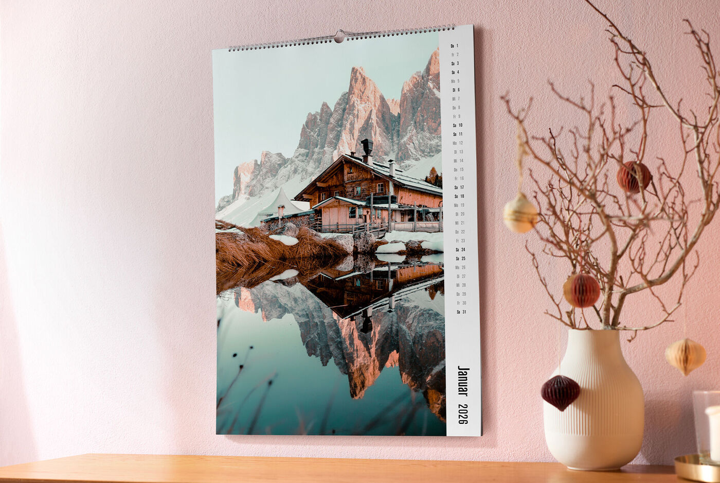 Ein CEWE Fotokalender zeigt im Januar ein stimmungsvolles Bergpanorama mit einer Hütte, die sich im klaren Wasser spiegelt.