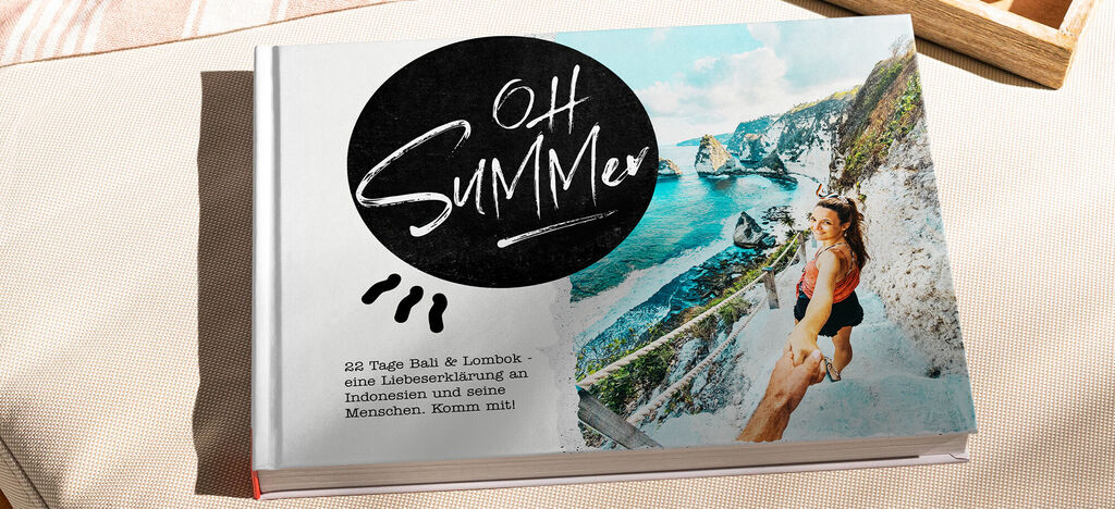 Ein CEWE FOTOBUCH mit dem Titel 'Oh Summer' liegt auf einem hellen Untergrund. Die Seite zeigt eine junge Frau, die am Rand einer Klippe mit Meerblick steht.
