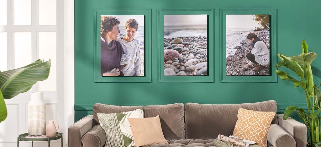 Drei schöne Bilder in Rahmen an grüner Wand über einem grauen Sofa. Die Bilder zeigen glückliche Momente mit Freunden und Familie.