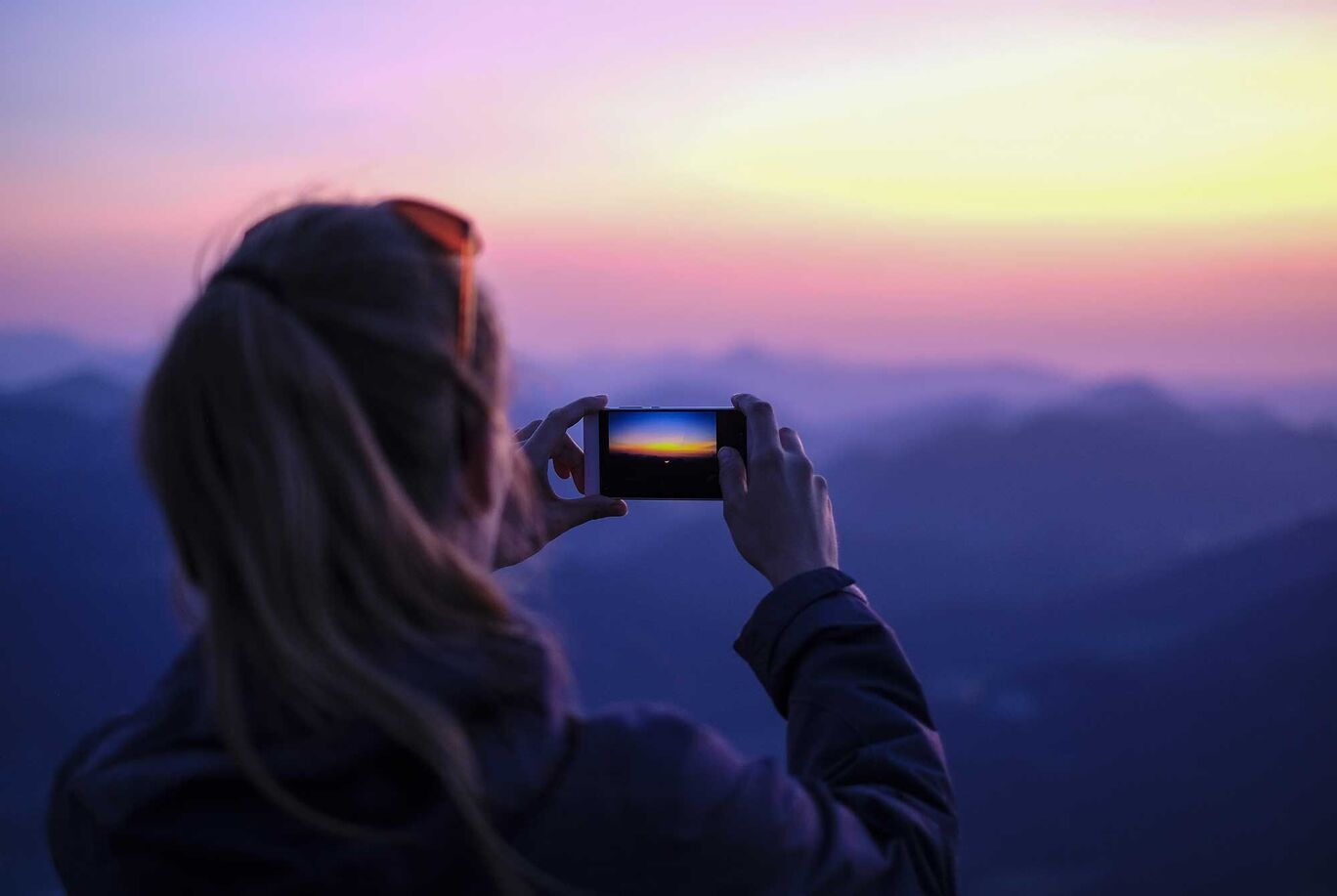 Eine Person fotografiert den Sonnenuntergang mit dem Handy.