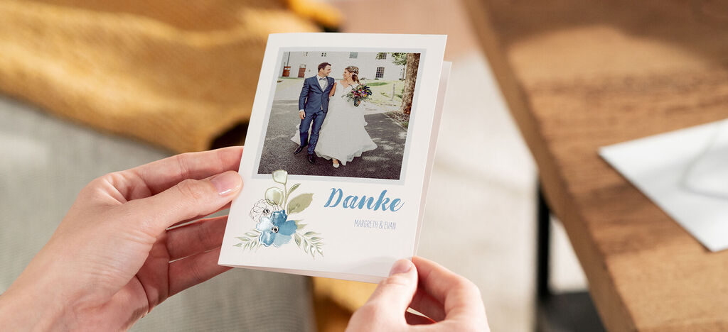 Eine Person hält eine wunderschöne Dankeskarte mit Blumenmotiv und Hochzeitsfoto in der Hand