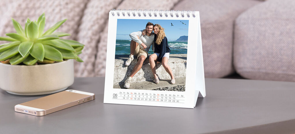 Ein Tisch mit einem kleinen Kalender, der ein fröhliches Foto von zwei Personen am Strand zeigt, sowie einem Smartphone.