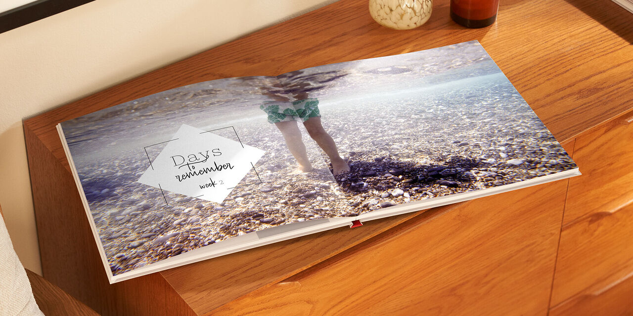 Ein offenes Fotobuch mit Erinnerungen an den Strand. Auf der Seite sieht man einen Fuß, der im Wasser steht, mit dem Text: 'days', 'in Erinnerungen', 'Unik'.