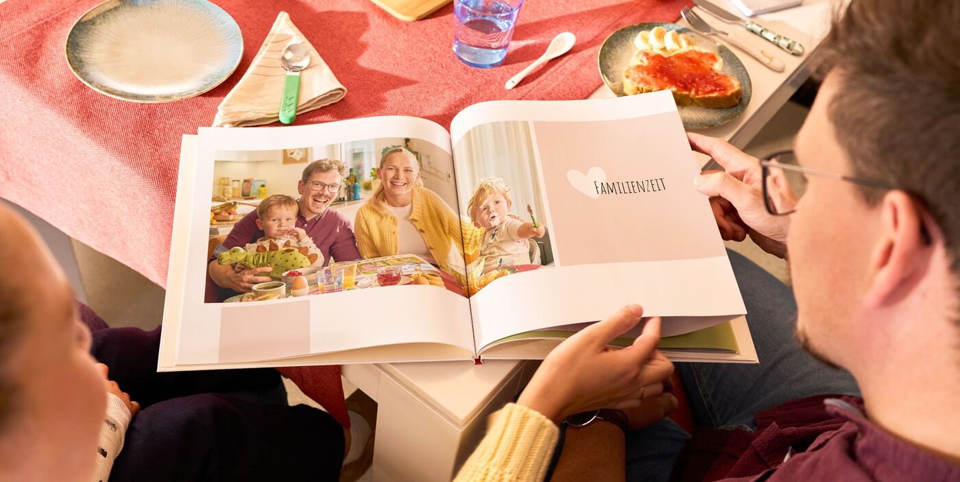 Eine Familie betrachtet gemeinsam ein CEWE FOTOBUCH am Esstisch.