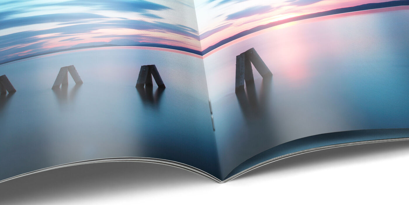 Aufgeschlagenes CEWE FOTOBUCH als Heft mit Rückstichbindung. Auf den Seiten ist eine Aufnahme eines Sonnenuntergangs.