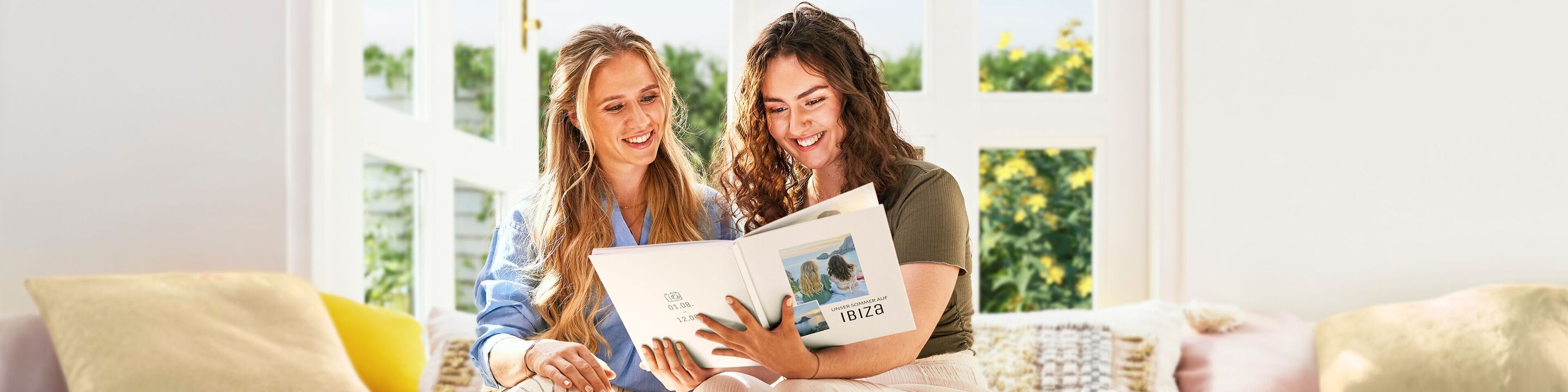Zwei Personen sitzen in einem hellen Raum und betrachten ein CEWE FOTOBUCH, sie wirken entspannt und glücklich