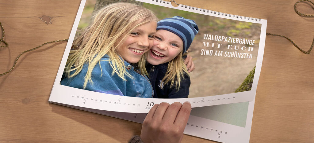 Eine Person blättert durch einen CEWE Fotokalender mit schönen Urlaubsbildern im Wald. Ein Zitat über Waldspaziergänge ist zu sehen.
