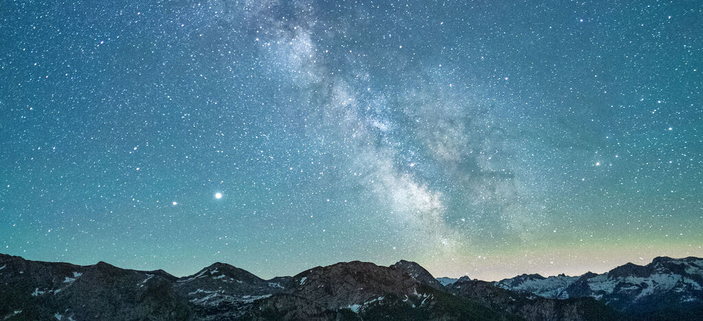 Ein nächtlicher Himmel voller Sterne über majestätischen Berggipfeln.