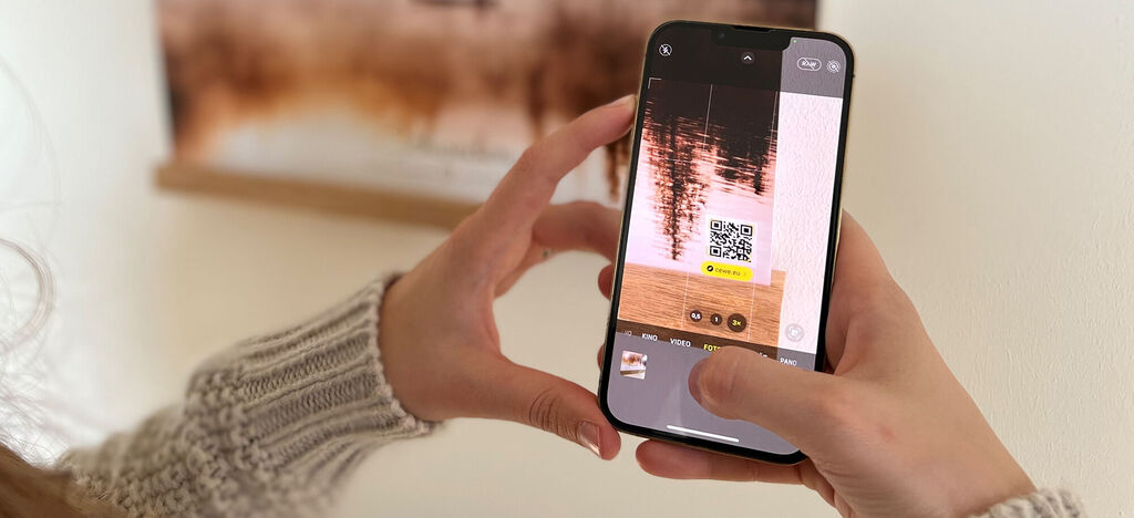 Person hält Smartphone mit QR-Code und bearbeitet ein Bild.