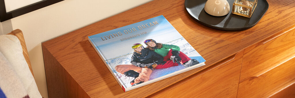 Ein CEWE FOTOBUCH liegt auf einem Tisch, es zeigt ein Paar mit Skiausrüstung auf der Vorderseite.