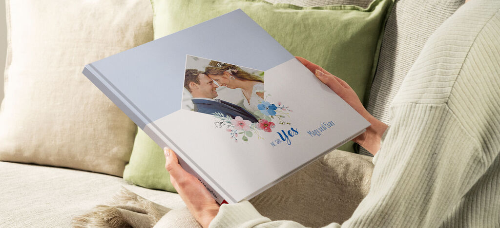Eine Person hält ein CEWE FOTOBUCH mit einem Hochzeitsmotiv in den Händen