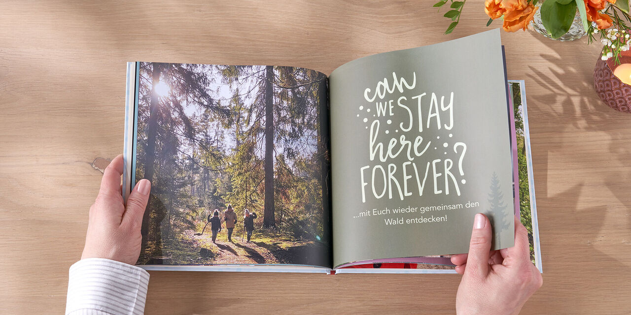 Zwei Personen gehen in einem Wald, während eine Hand ein CEWE FOTOBUCH mit schönen Erinnerungen hält