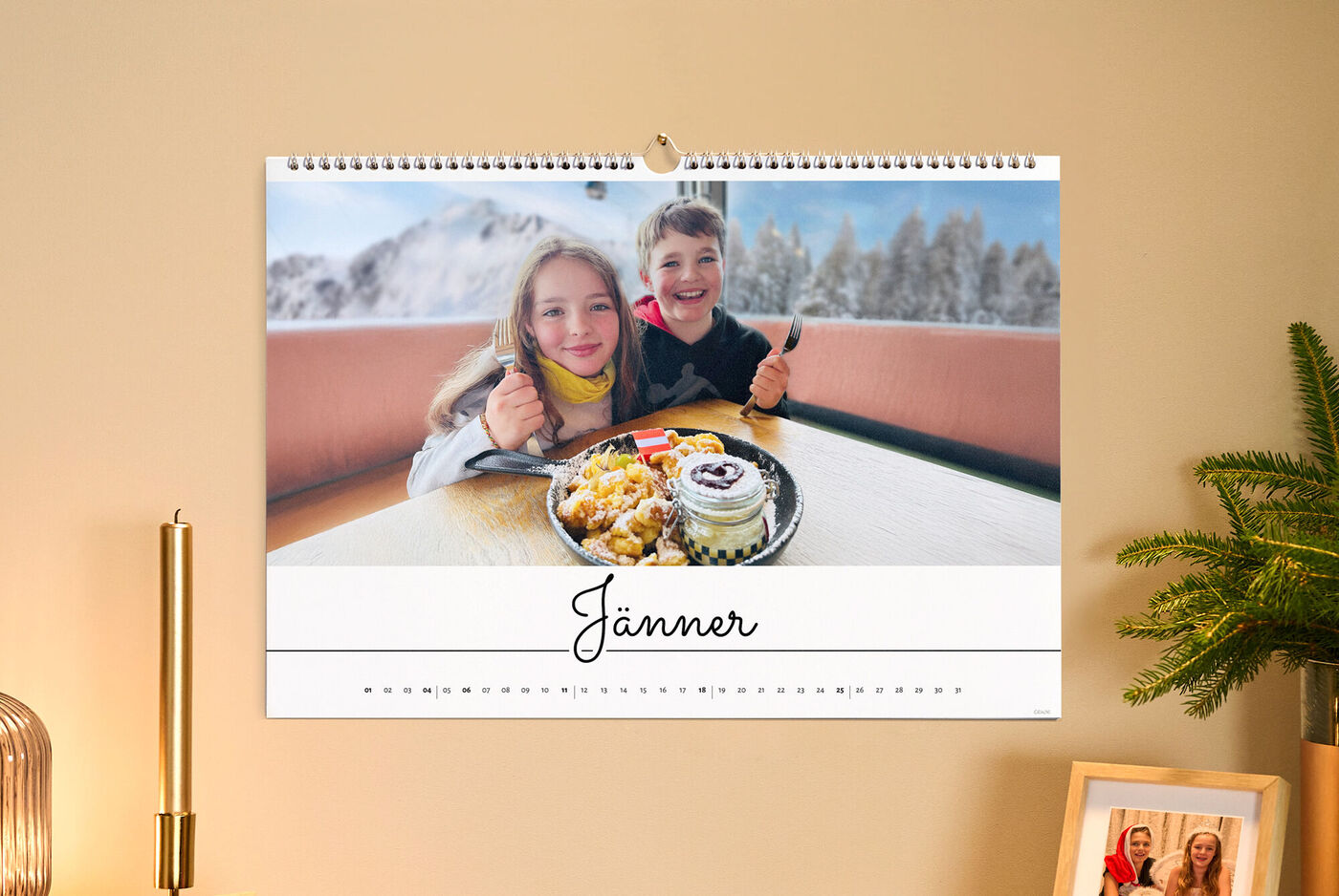 Weihnachtszauber an der Wand: Fotokalender „Jänner“ mit zwei Kindern und Dessert vor verschneiter Bergkulisse, warmes Licht und Tannengrün.