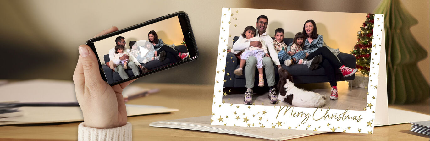 Eine Familie sitzt glücklich auf einem Sofa und hält Weihnachtskarten. Im Hintergrund steht ein schöner Weihnachtsbaum.