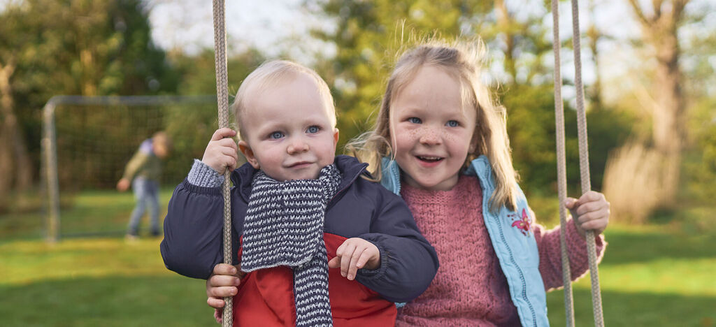 Zwei fröhliche Kinder schwingen gemeinsam auf einer Schaukel im Freien.