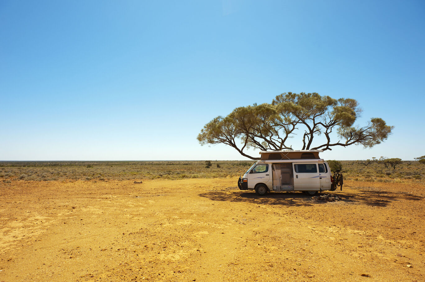 Ein Camper unter einem Baum in der Wüste mit blauem Himmel