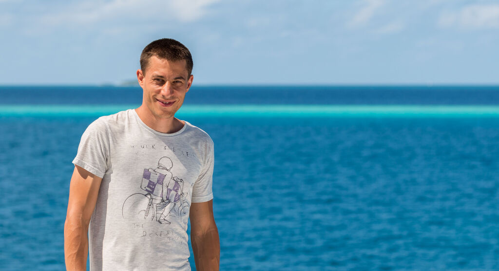 Junger Mann steht am Strand mit Meer im Hintergrund