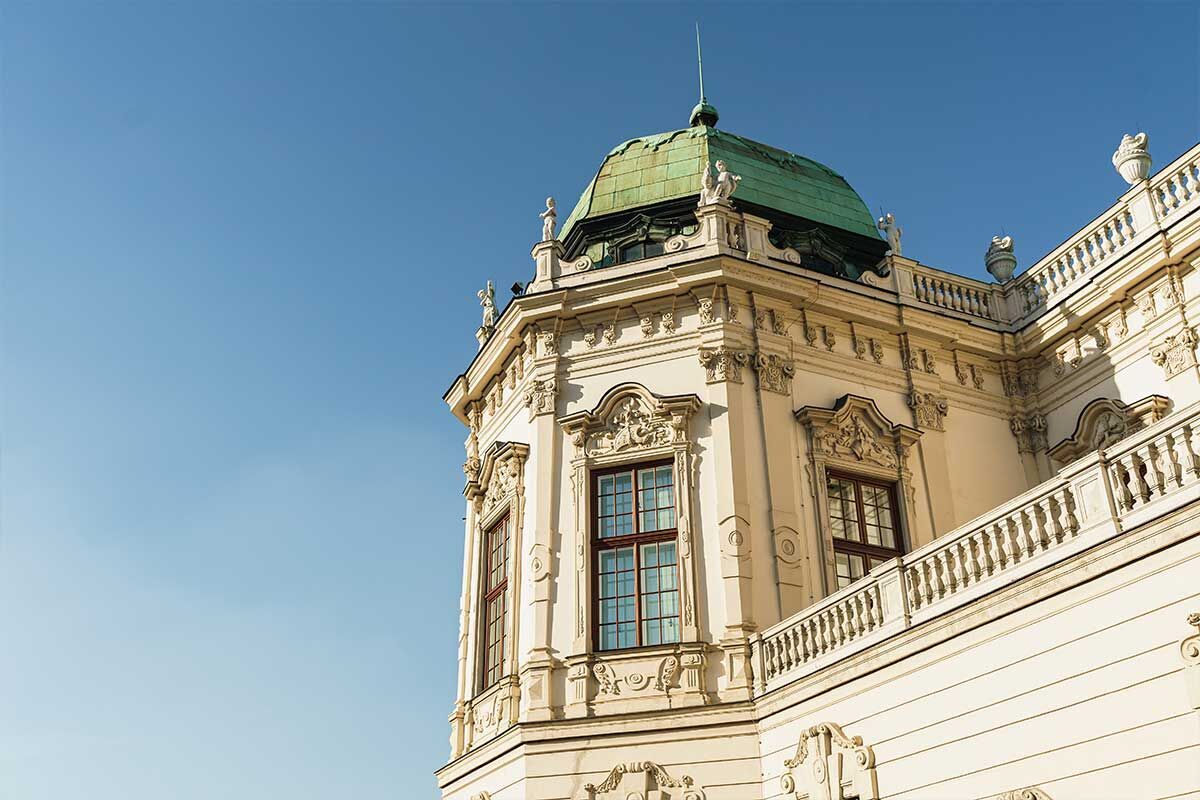 Detailansicht eines historischen Gebäudes mit grünem Dach und geschmückten Fenstern vor klarem Himmel