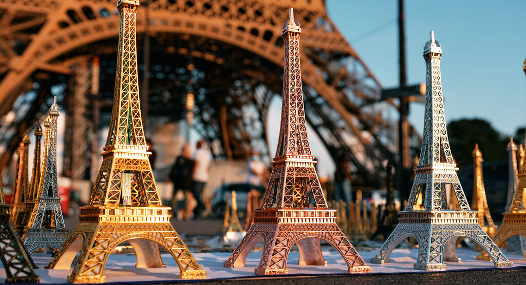 Miniaturmodelle des Eiffelturms in Gold und Silber vor dem echten Eiffelturm.