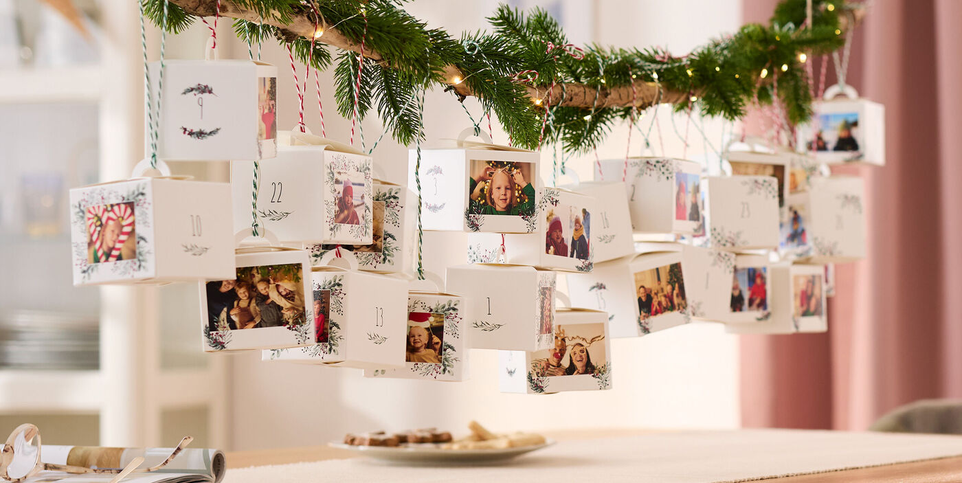 Ein dekorativer Adventskalender aus 24 einzelnen Schachteln mit Familienfotos aufgehangen an einem Tannenzweig.