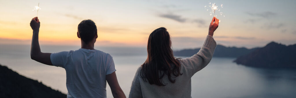 Paar genießt den Sonnenuntergang am Meer und zündet Wunderkerzen an.