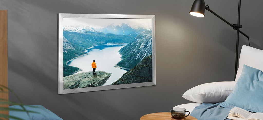 Eine Person in orangefarbener Jacke steht auf einem Felsen und blickt auf einen majestätischen See und Berge im Hintergrund