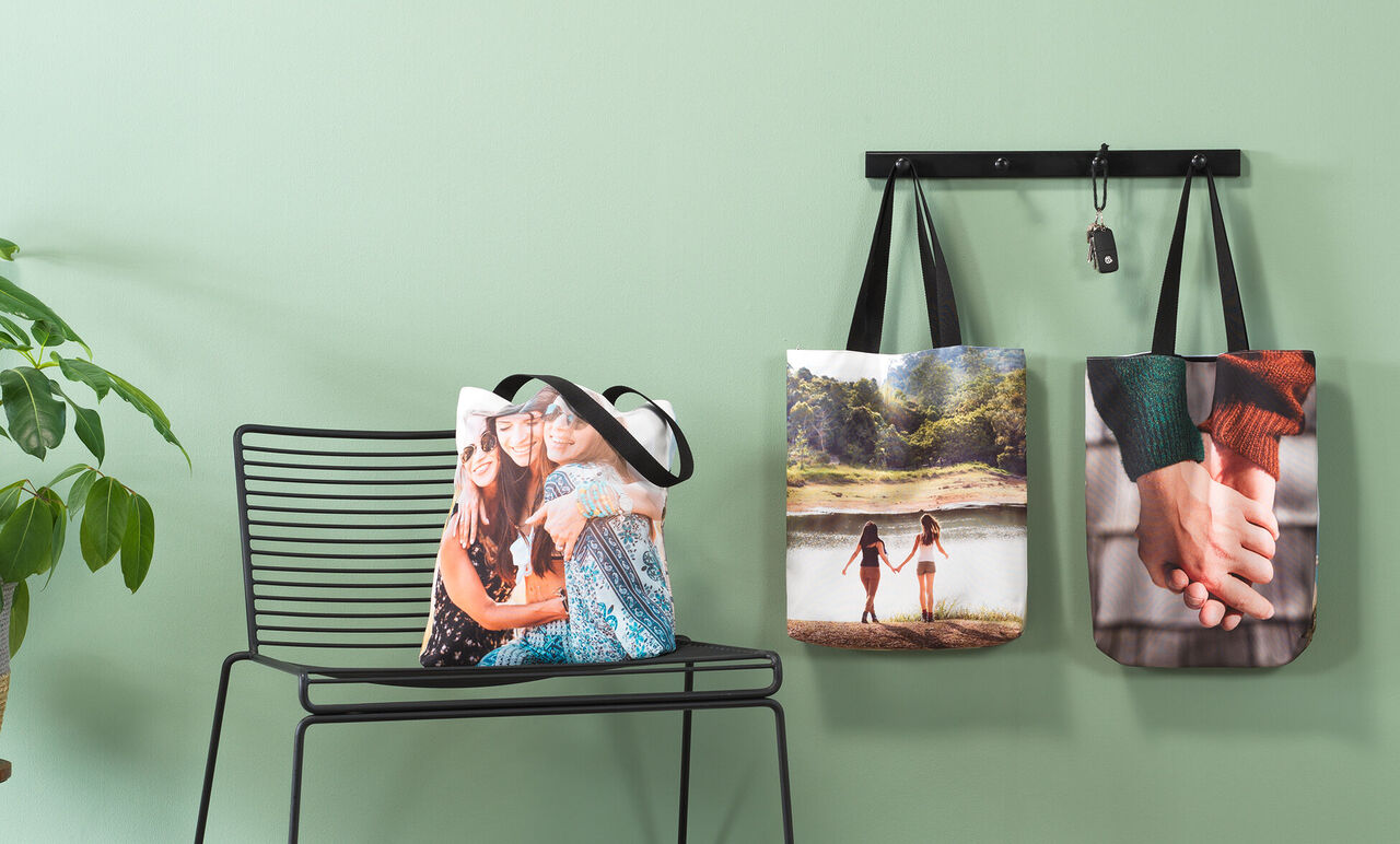 Drei kreative Taschen mit persönlichen Fotomotiven hängen an einem Wandregal. Eine zeigt zwei Freundinnen, eine andere eine verträumte Landschaft und die dritte Händchen haltende Paare